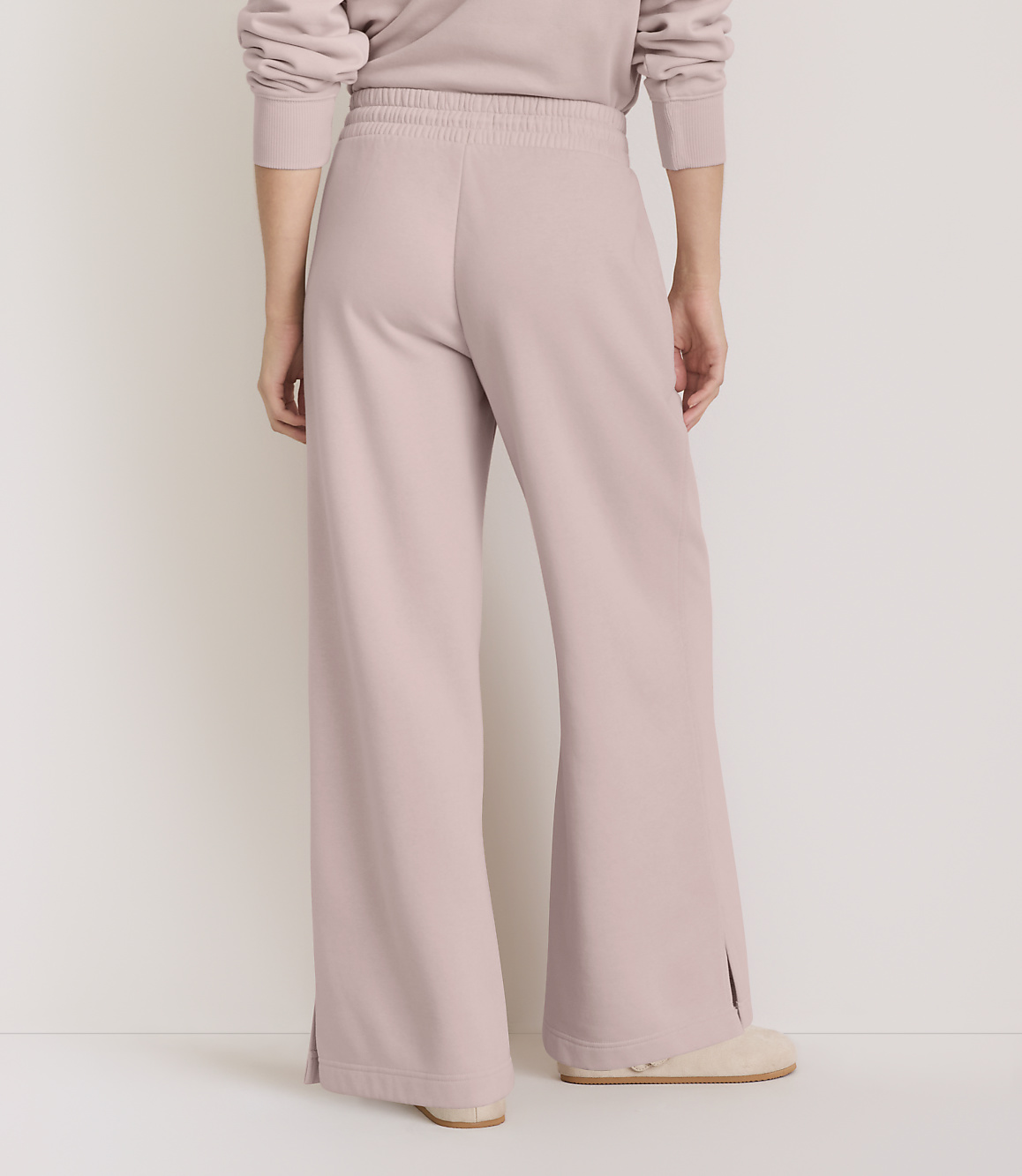 A person wearing light pink wide-leg sweatpants with side slits stands on a light-colored floor against a plain white background.