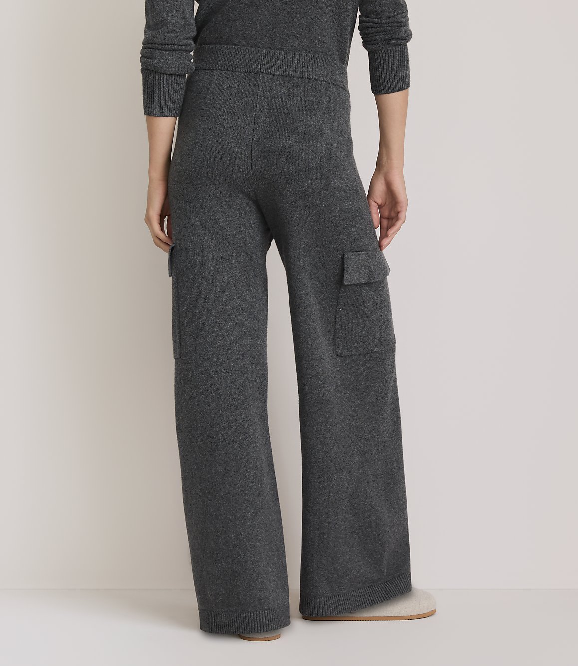 A person wearing dark gray knit cargo pants stands on a light-colored floor, with a plain, light background.