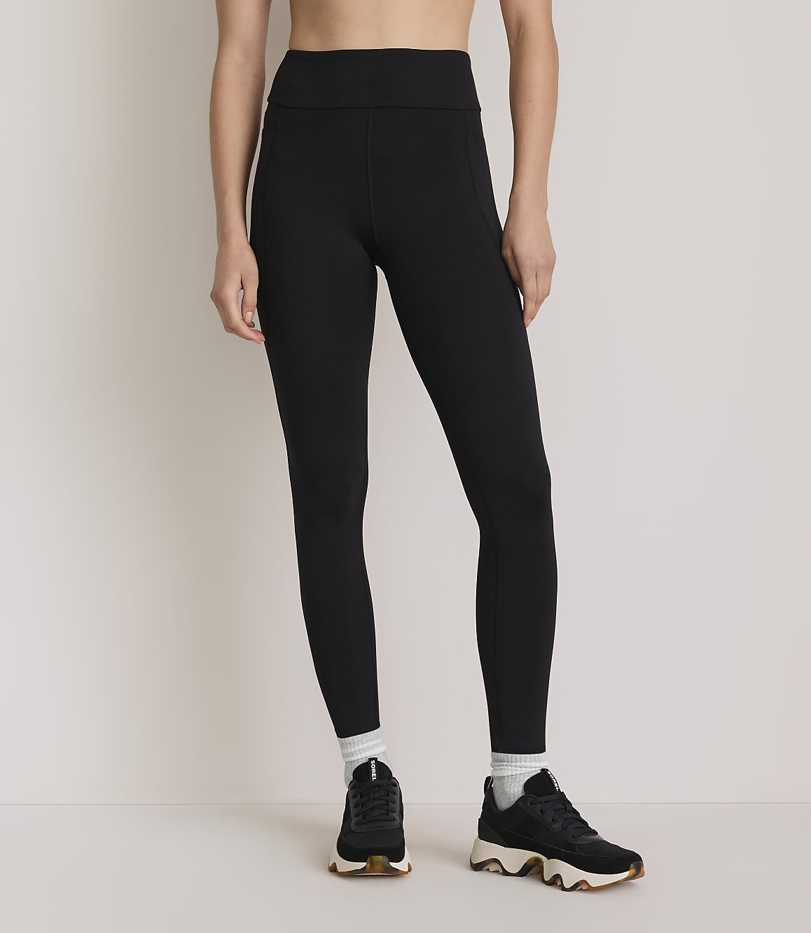 A person wearing black leggings, white socks, and black sneakers stands against a plain white background.