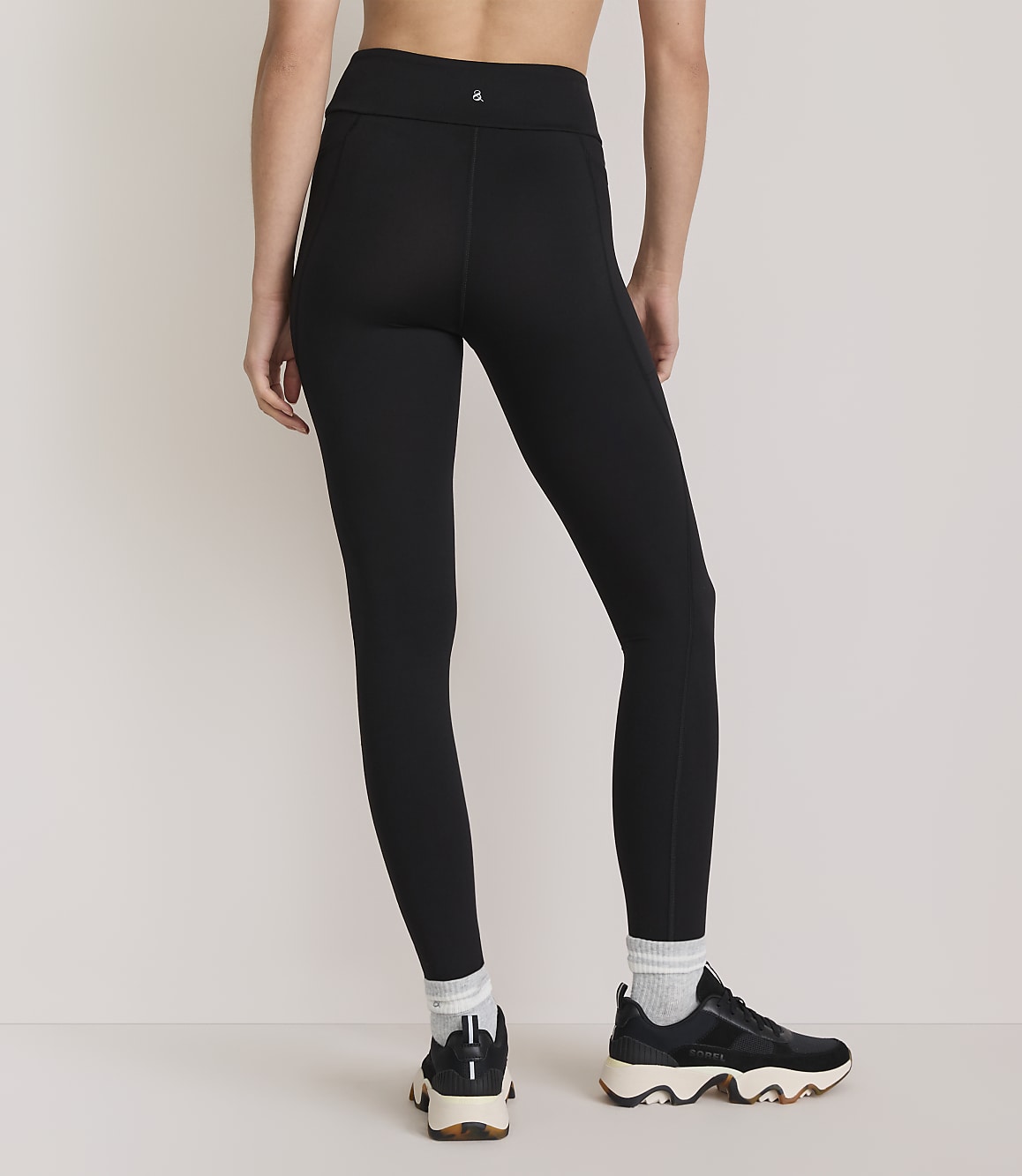 A person wearing black leggings and athletic shoes stands against a plain, light-colored background.