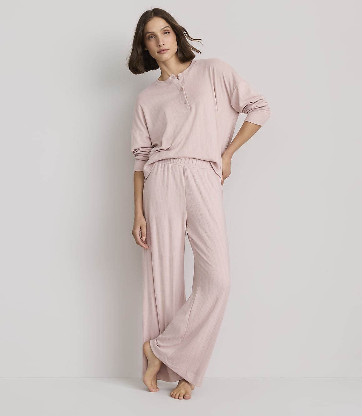 A woman in pink pajamas stands against a plain, light gray background.