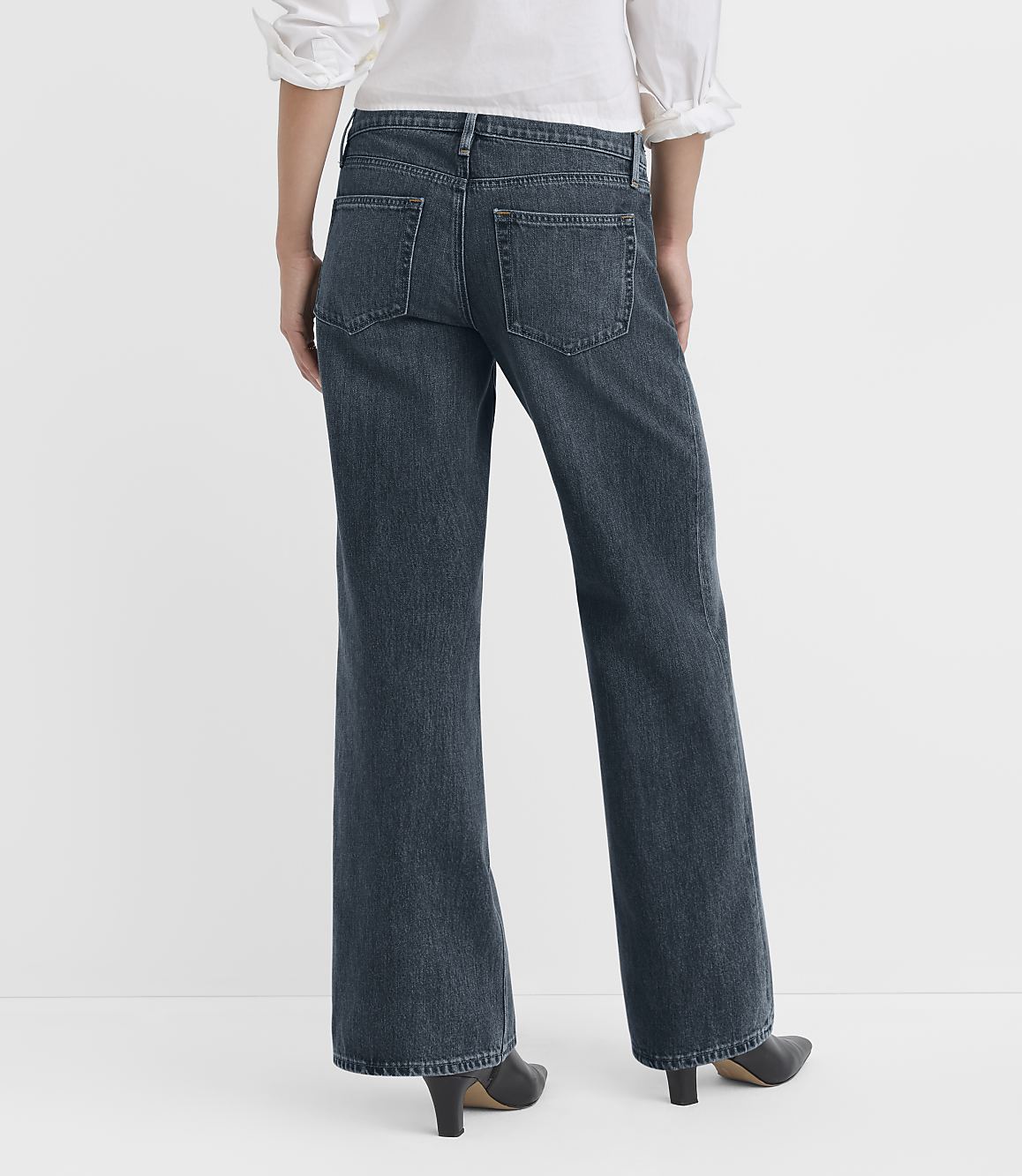 A person wearing dark wash flared jeans and a white top stands against a plain white background.