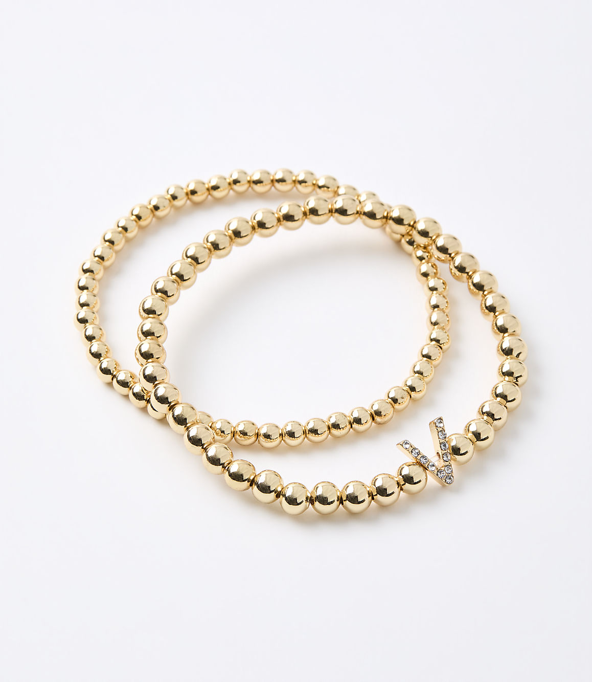 Two gold beaded bracelets, one with a diamond-encrusted "V" charm, rest on a plain white background.