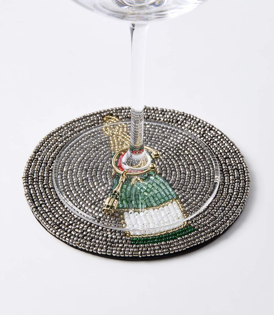 A beaded coaster with a festive bottle charm encircles the stem of a wine glass against a plain white background.
