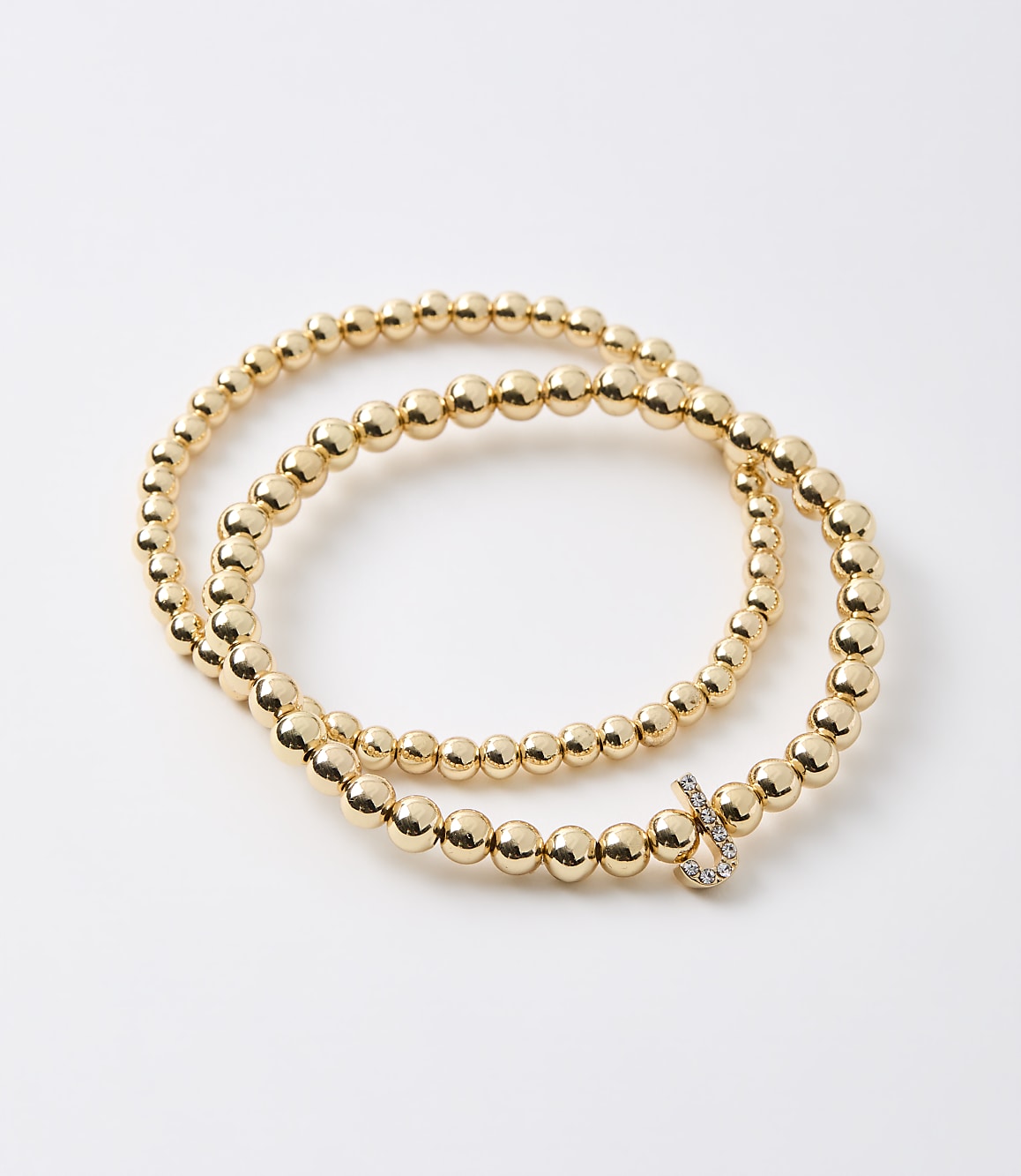 A gold beaded bracelet with a diamond-encrusted clasp rests on a plain white background.