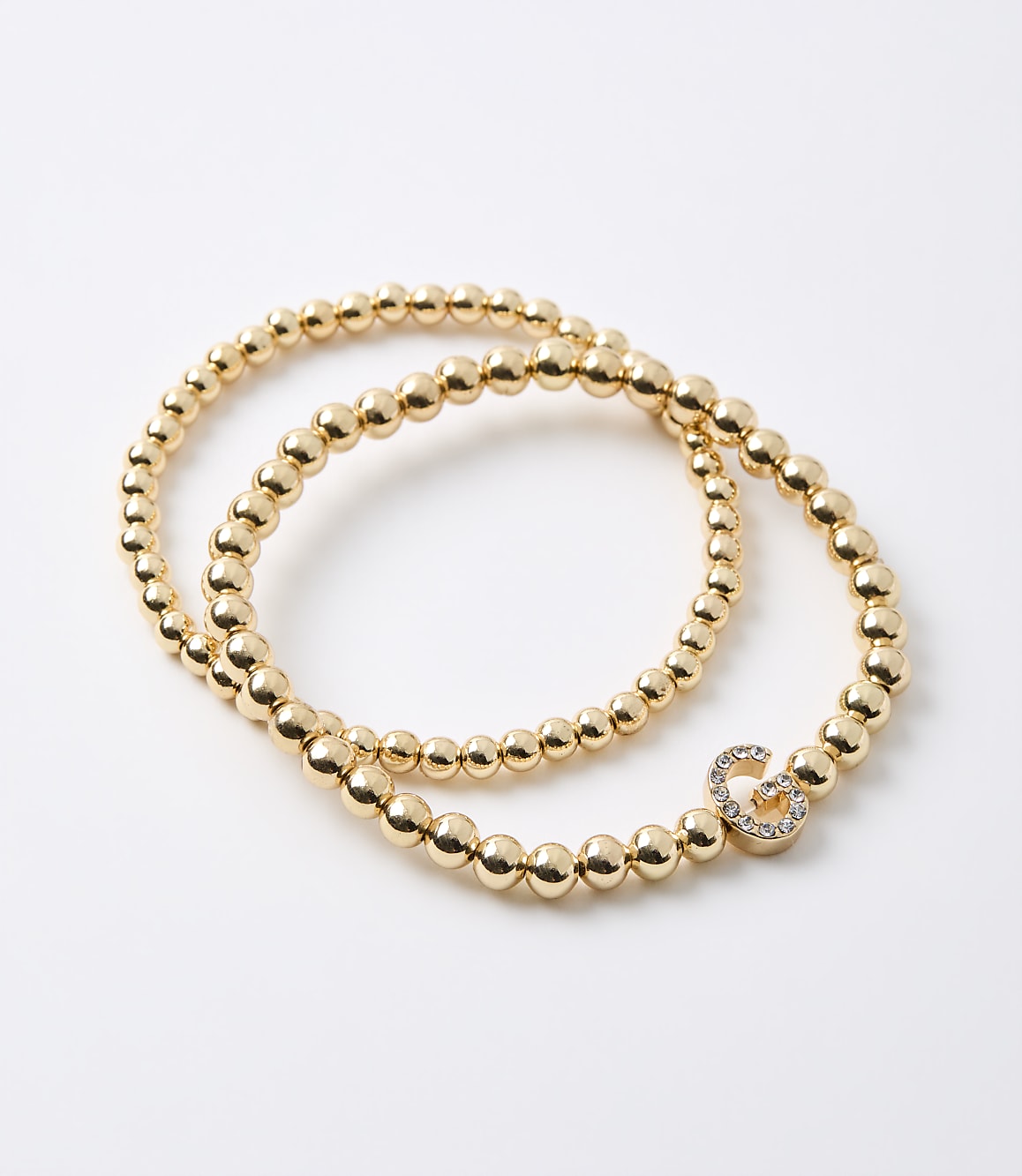 Two gold beaded bracelets, one with a diamond-encrusted infinity charm, lie on a plain white background.