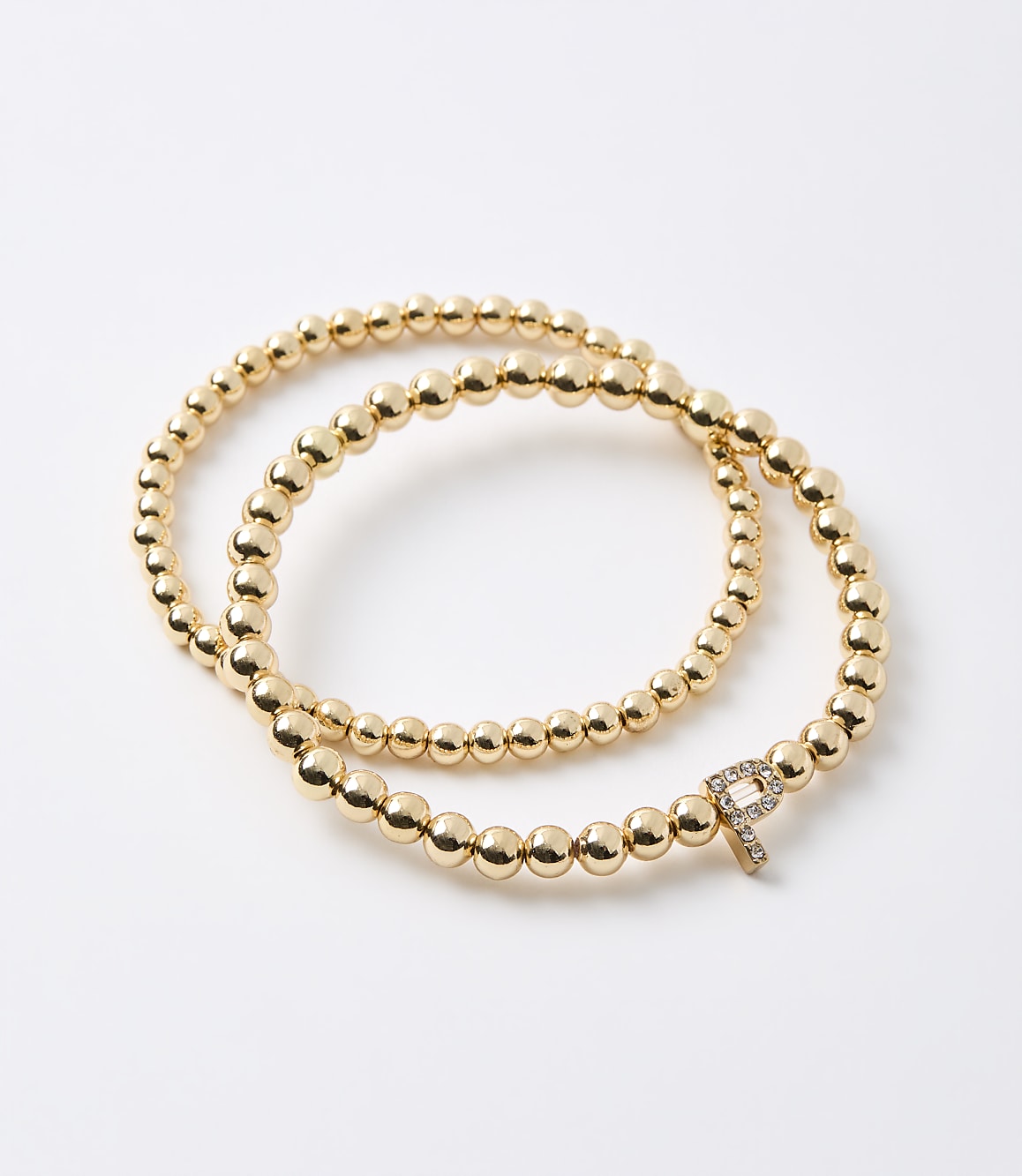 A gold beaded bracelet with a diamond-encrusted "P" charm is laid out on a white background.