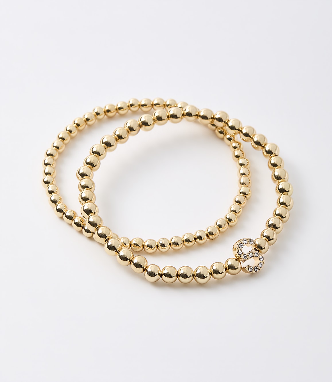 Two gold beaded bracelets, one with a sparkling number 8 charm, lie on a plain white background.