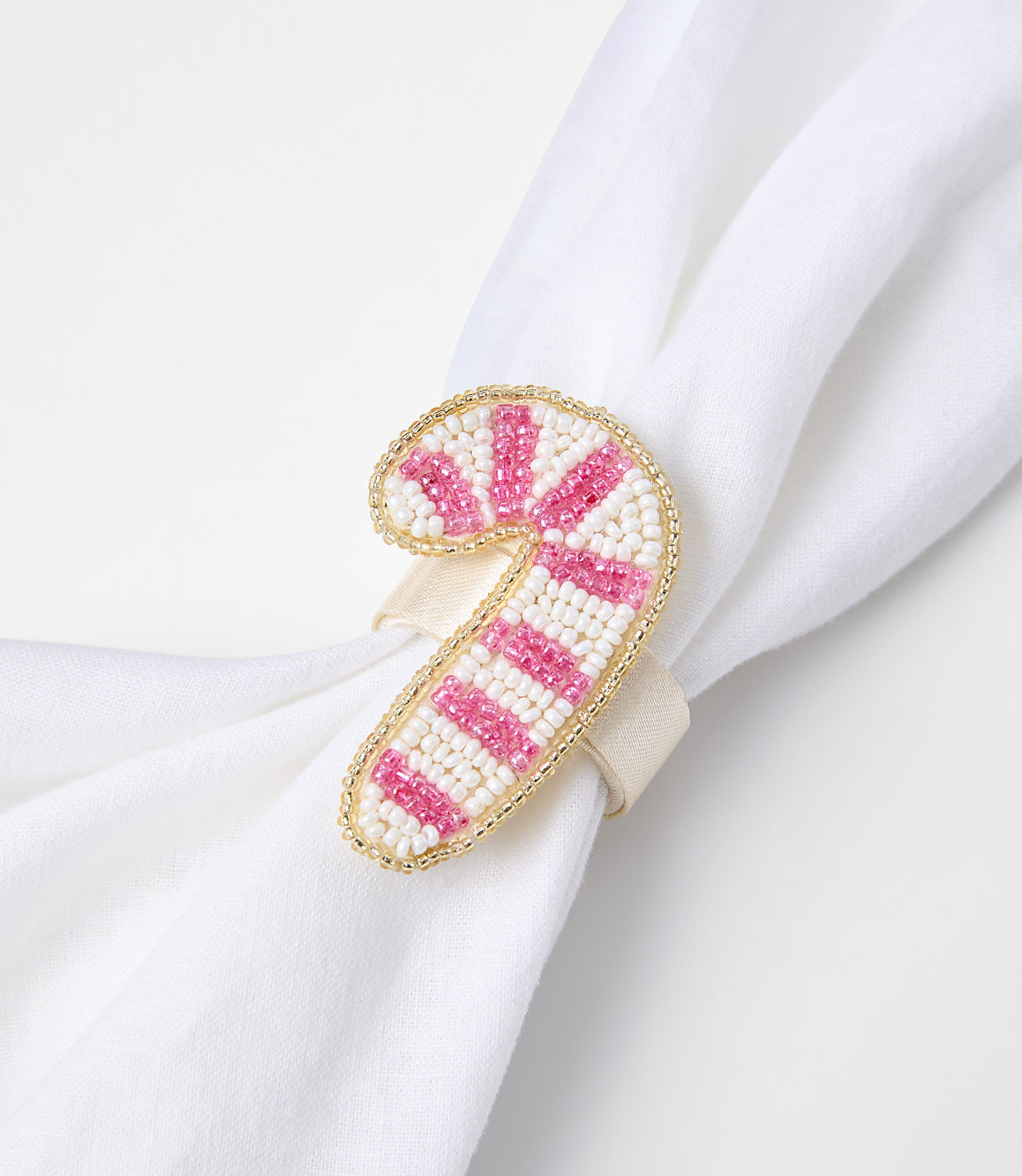 A beaded candy cane napkin ring with pink and white stripes adorns a white cloth napkin against a plain background.
