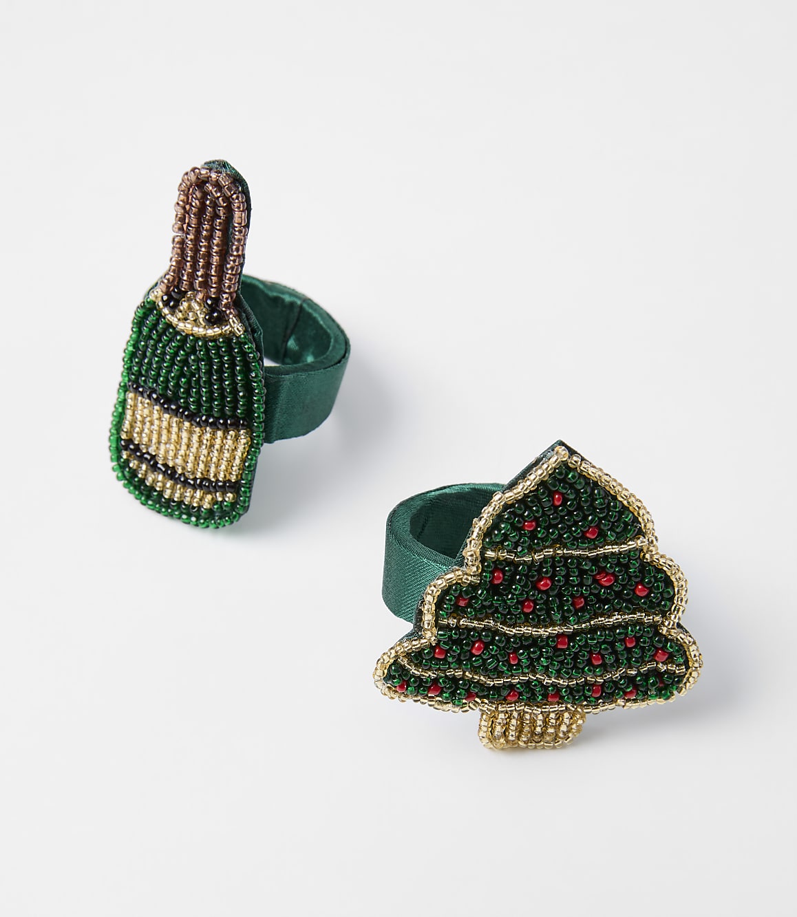 Two beaded Christmas-themed napkin rings, one shaped like a champagne bottle and the other like a Christmas tree, rest on a plain white background.