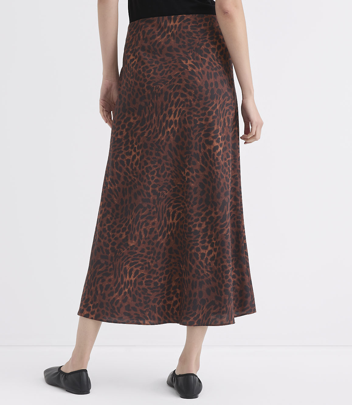 A person wearing a brown leopard-print skirt and black flats stands against a plain white background.