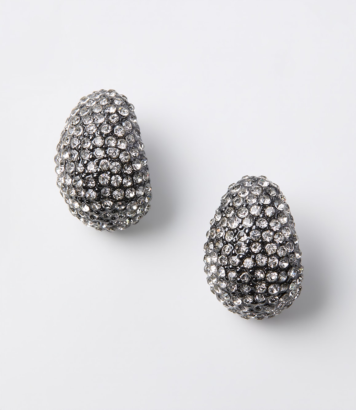 Two oval-shaped, crystal-encrusted earrings rest on a plain white background.