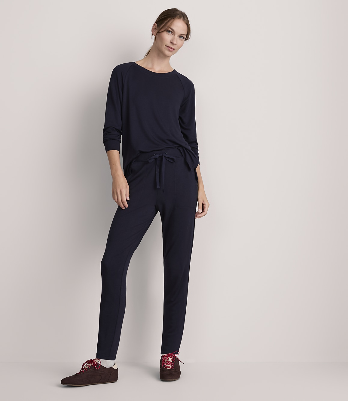 A woman in navy loungewear stands against a plain, light-colored wall.