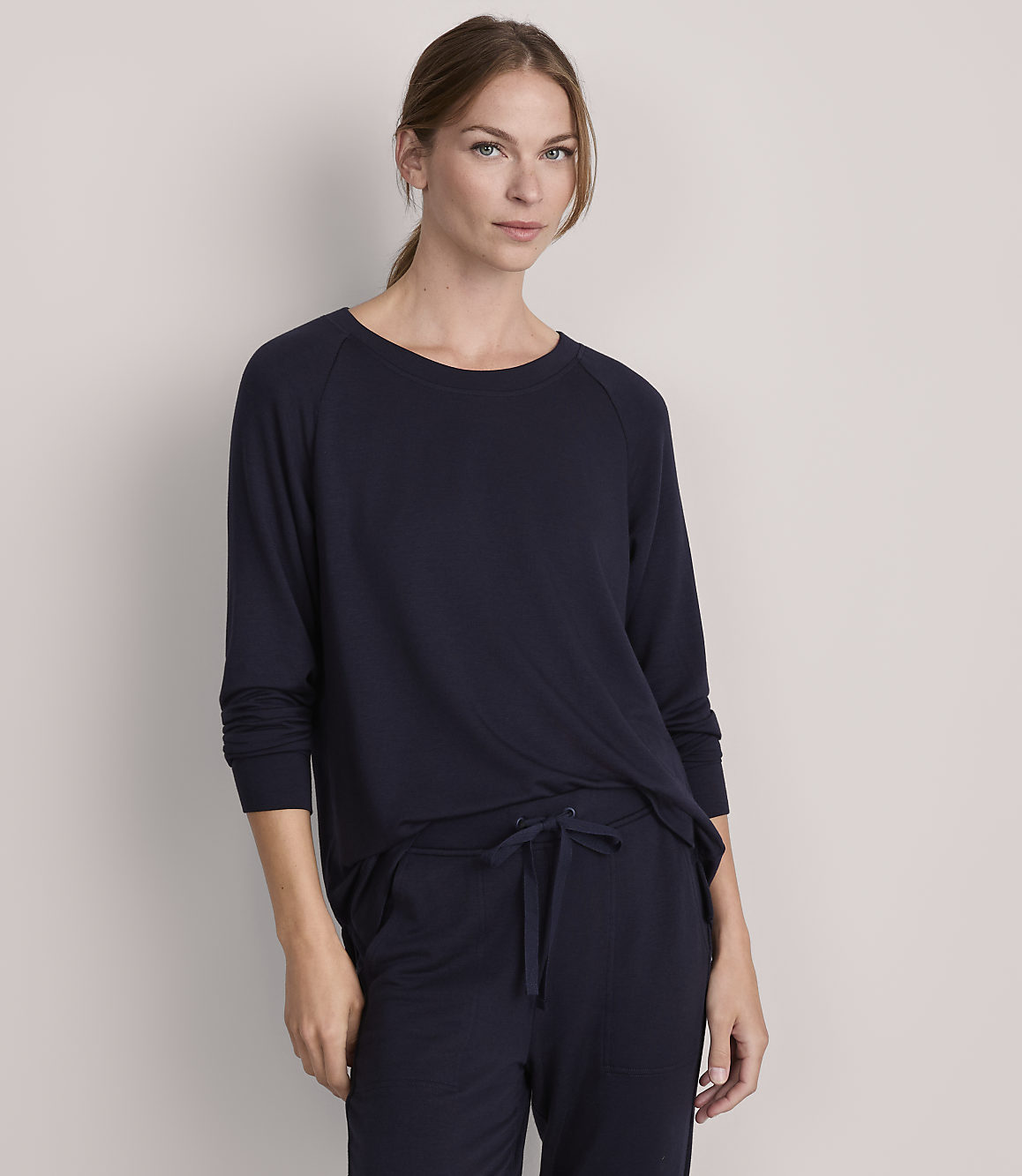 A woman in a navy blue long-sleeved shirt and matching pants stands against a plain gray background.