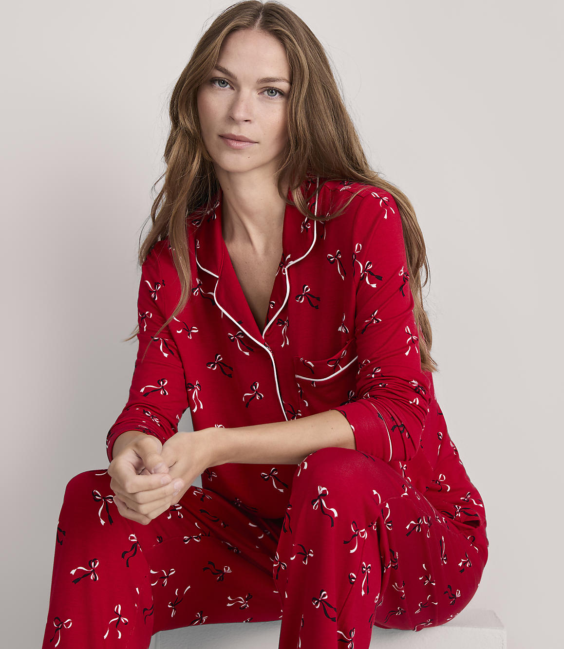 A woman in red pajamas with a bow pattern sits against a plain gray background.