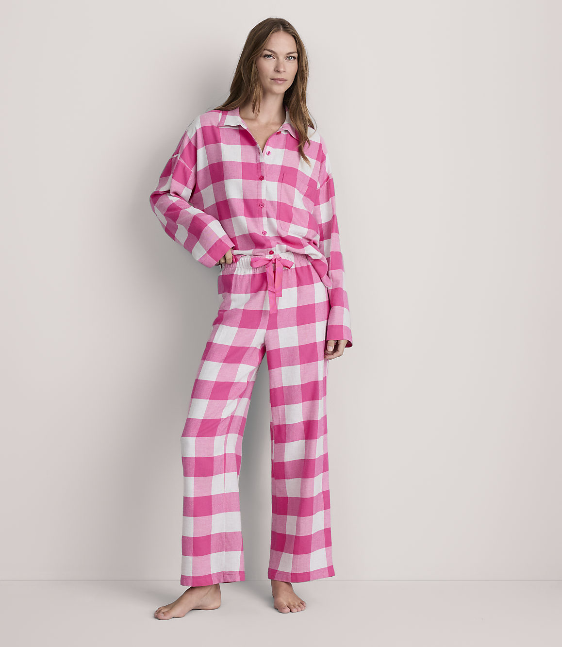 A woman stands in pink and white checkered pajamas against a plain white background.