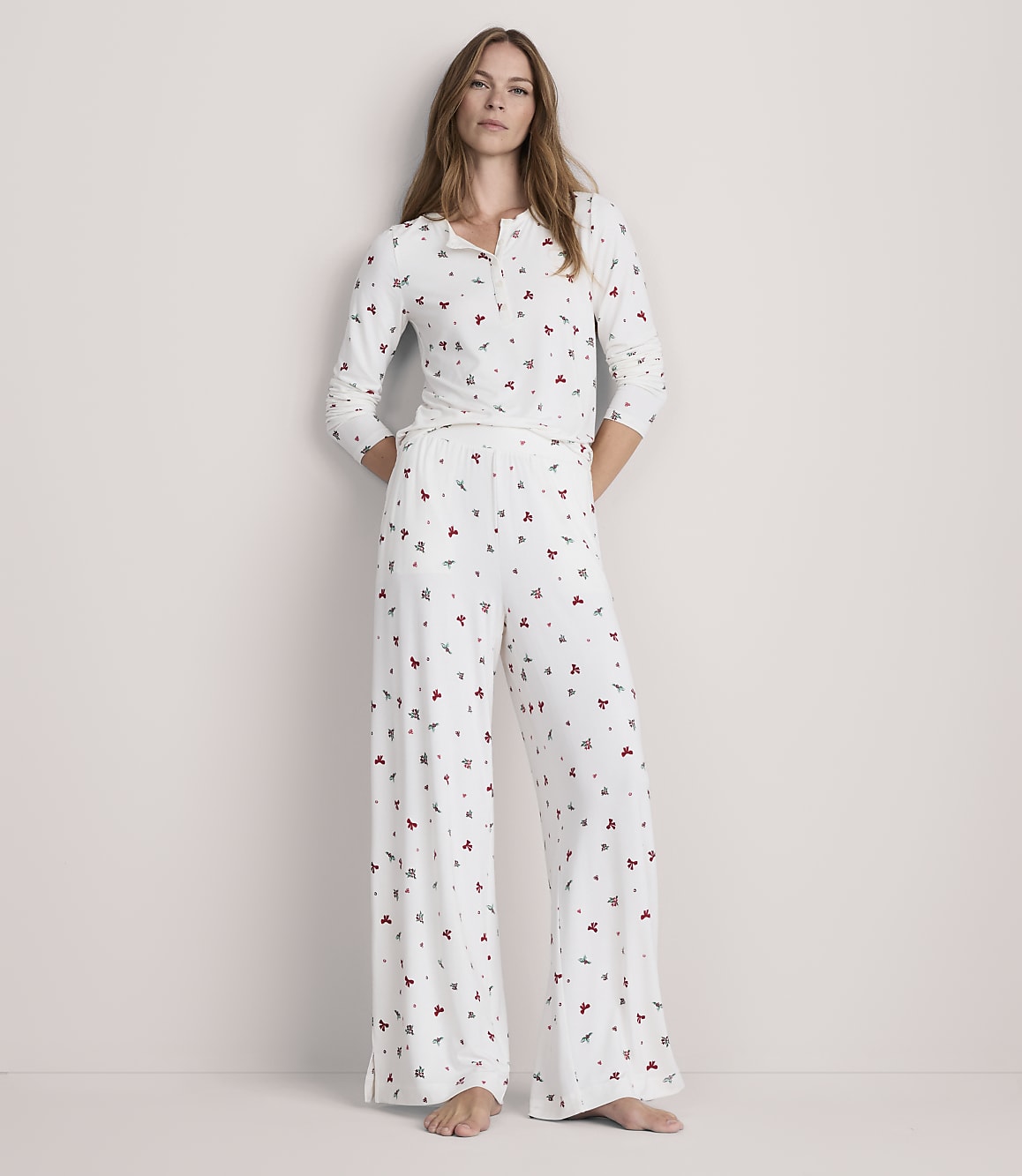 A woman stands in a white pajama set with a subtle heart pattern, against a plain, light-colored background.
