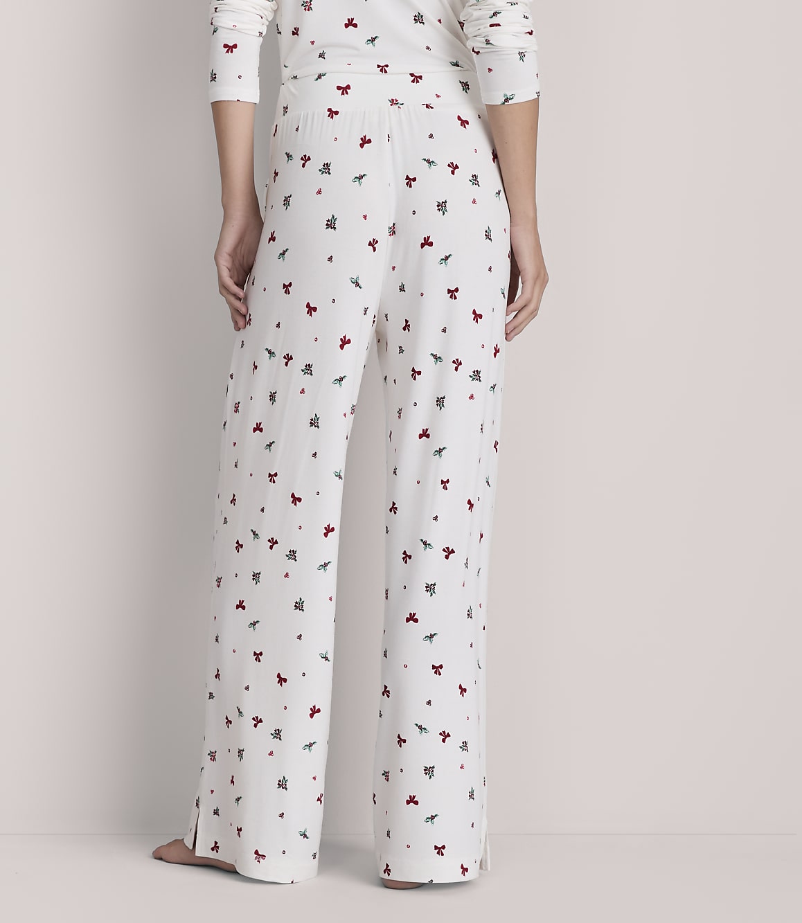 A person stands in white pajamas with a red and green holly pattern, against a plain, light-colored background.