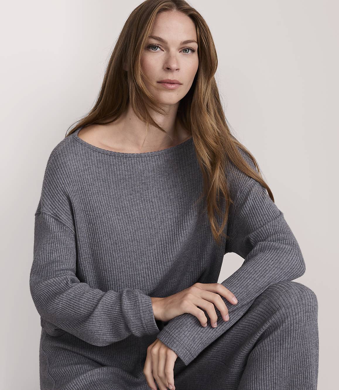 A woman in a grey ribbed sweater and pants poses against a plain, light background.