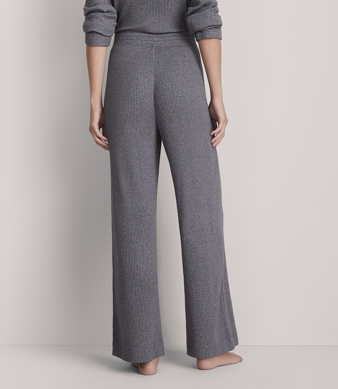 A person wearing grey ribbed pajama pants stands against a plain grey background.