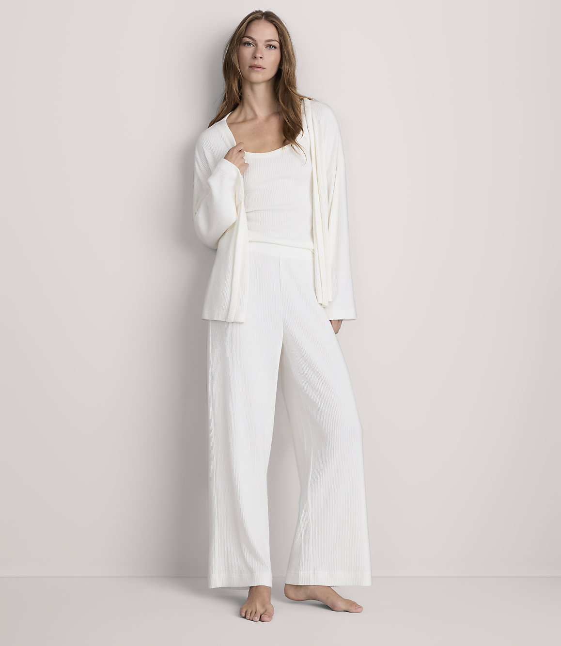 A woman in white pajamas stands against a plain, light-colored wall.