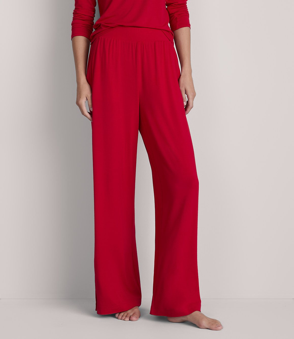A person stands in red pajama pants and a matching top against a plain, light gray background.
