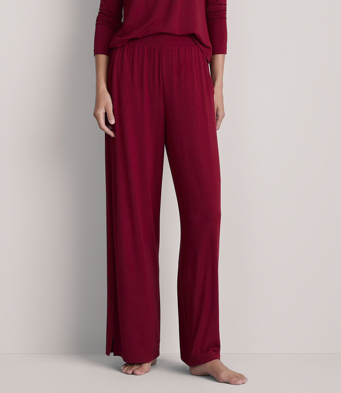 A person stands in loose-fitting burgundy pajamas against a plain, light gray background.