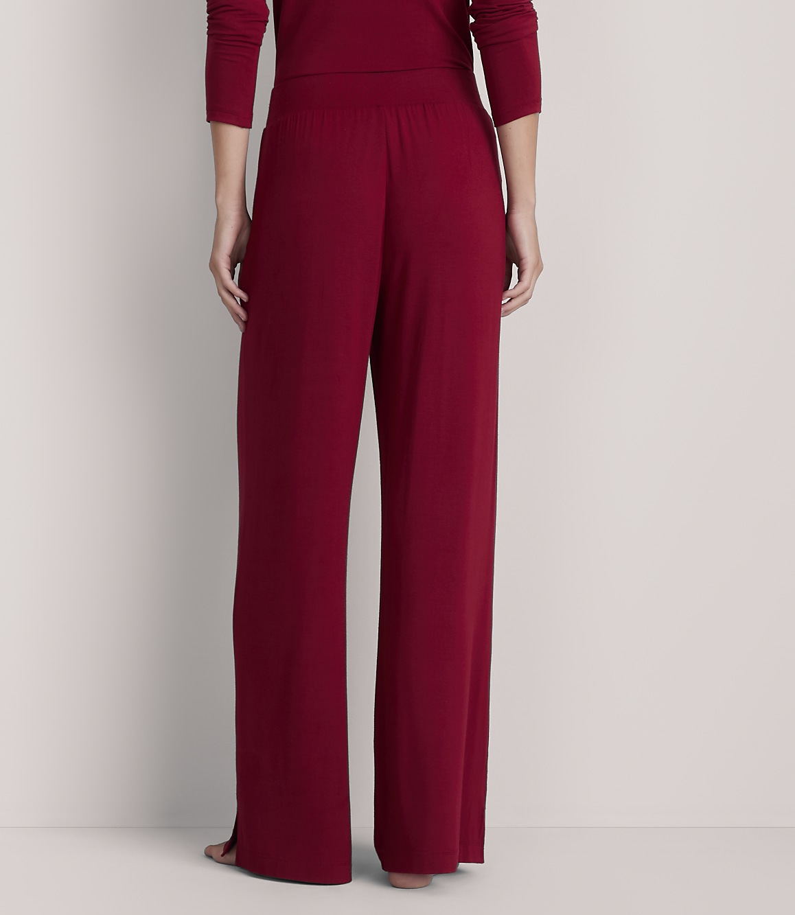 A person stands in loose-fitting, dark red pajama pants in the foreground, against a plain, light-colored background.