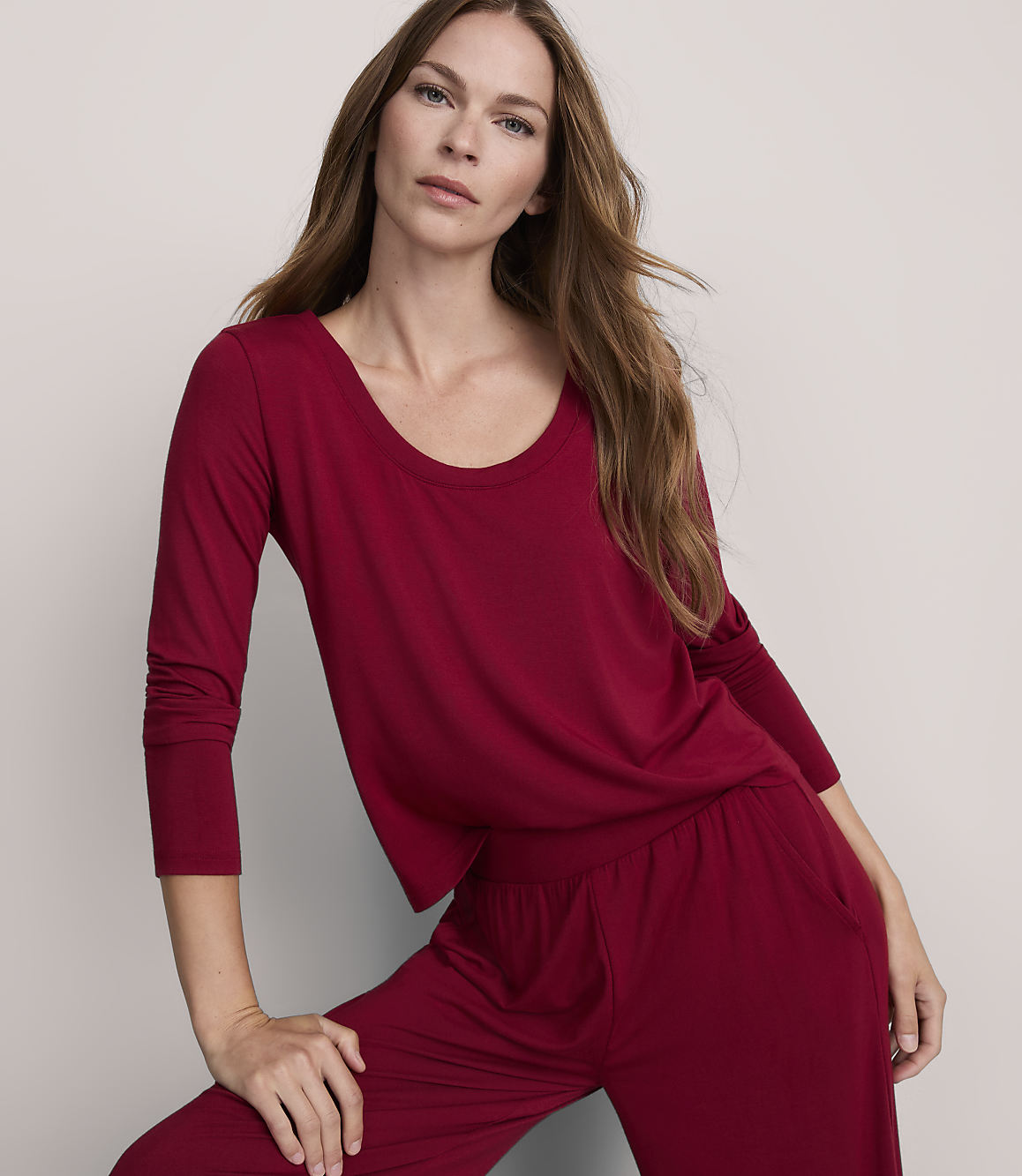 A woman in a maroon pajama set poses against a plain gray background.