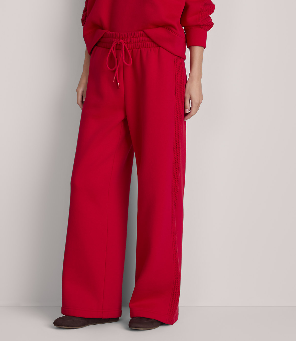 A person wearing bright red wide-leg sweatpants and dark shoes stands against a plain, light gray background.