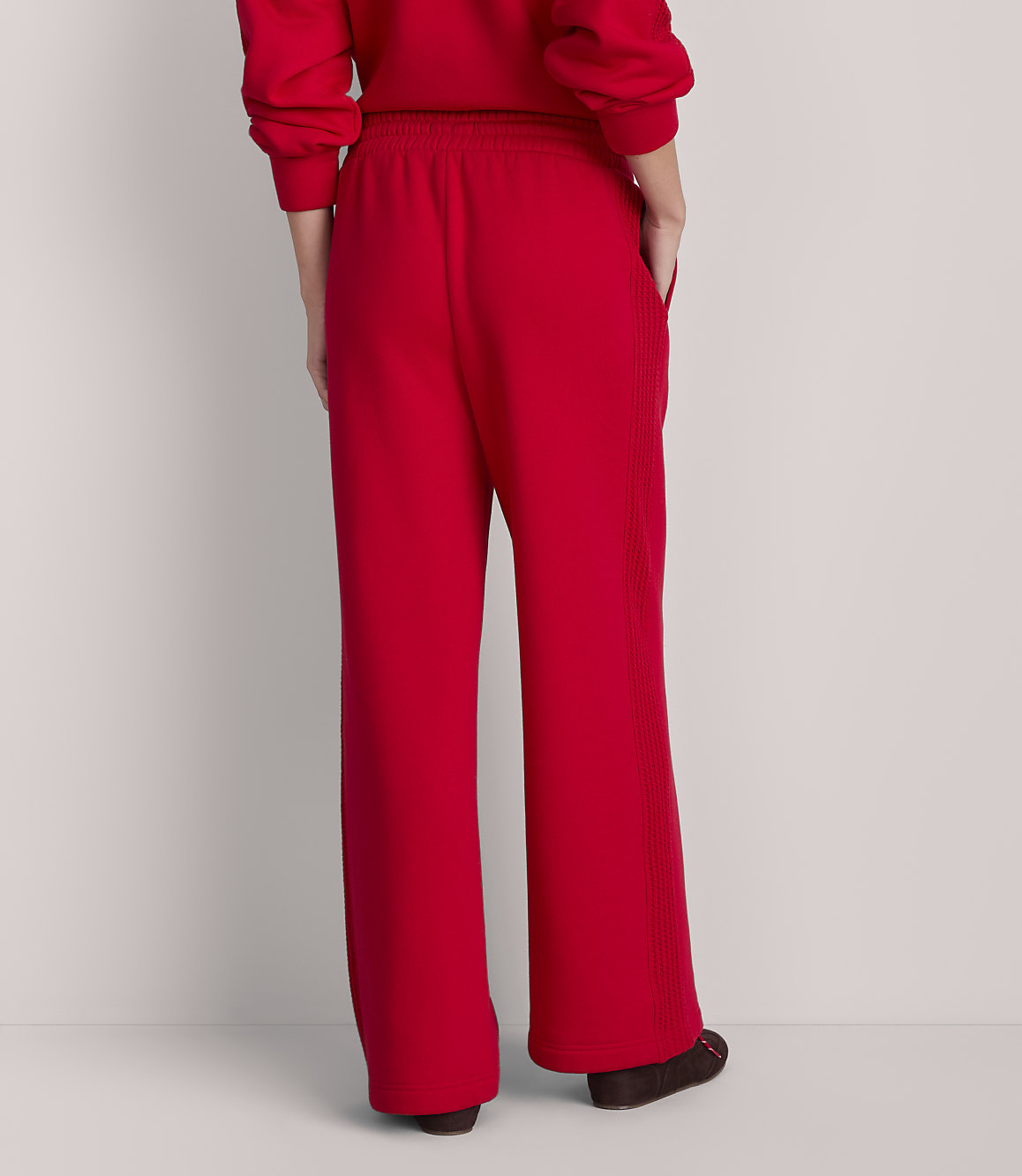 A person wearing red sweatpants and a matching top stands against a plain, light-colored background.