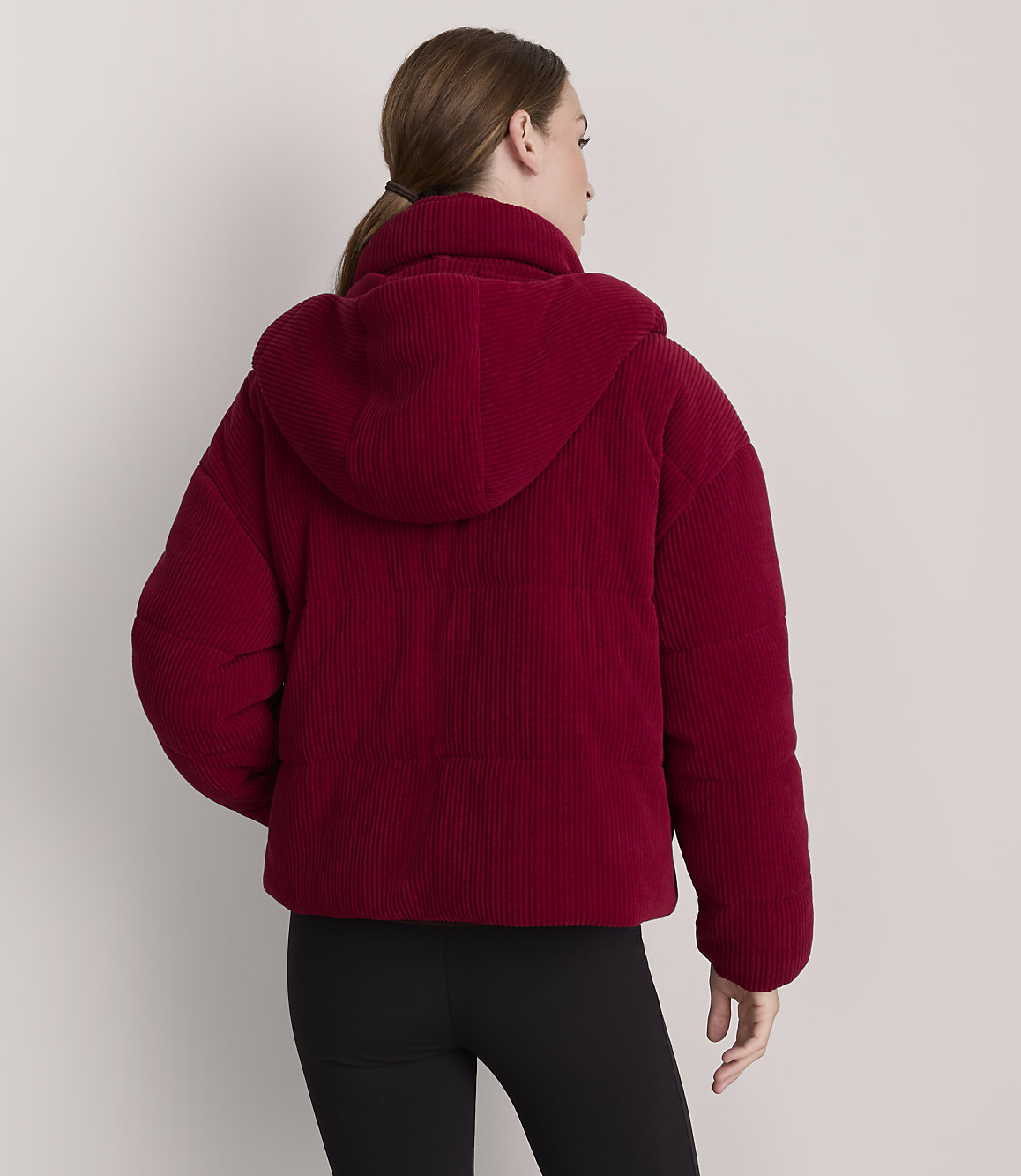 A woman in a red corduroy puffer jacket stands against a plain white background.