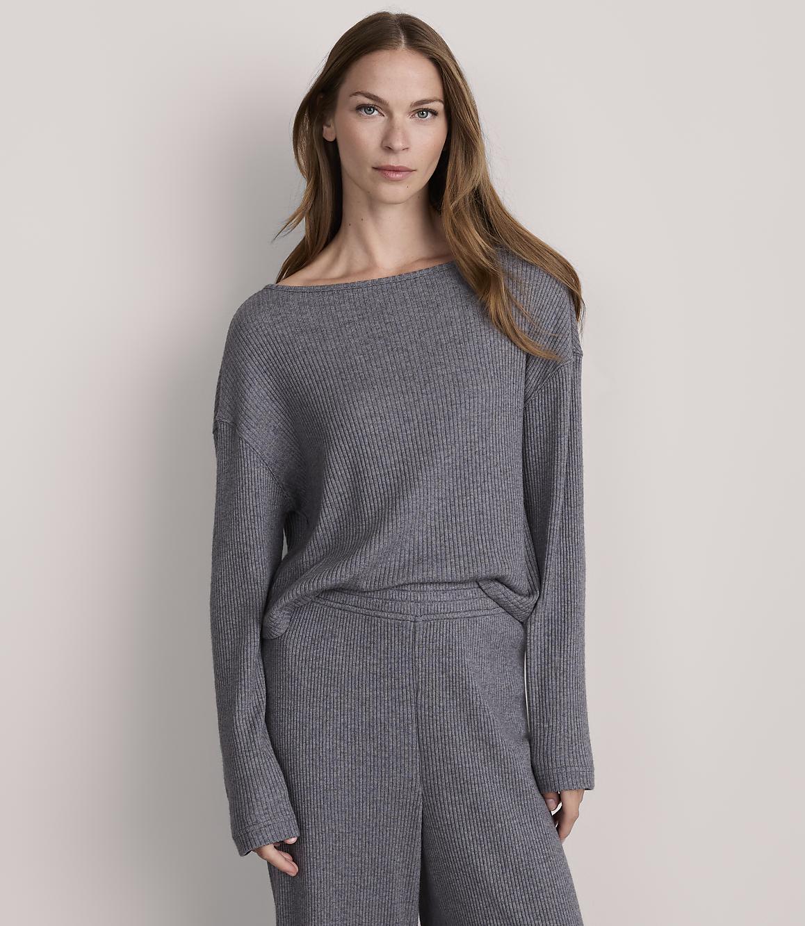 A woman in a grey ribbed sweater and pants stands against a plain grey background.
