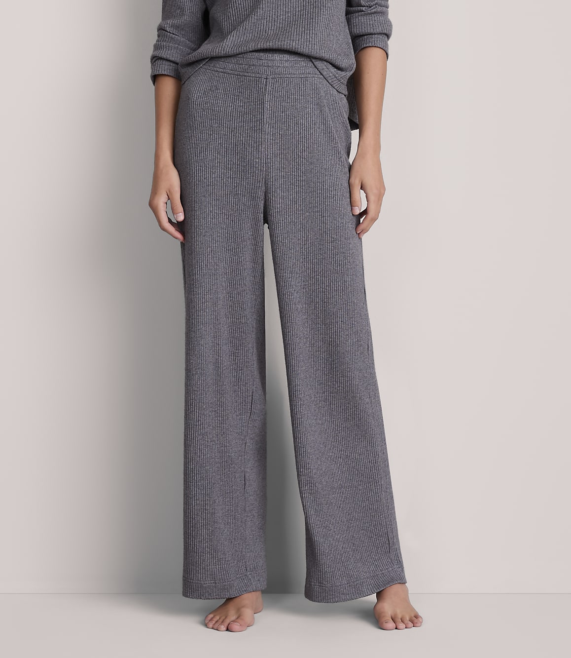A person stands in ribbed gray wide-leg pants and a matching top against a plain gray background.