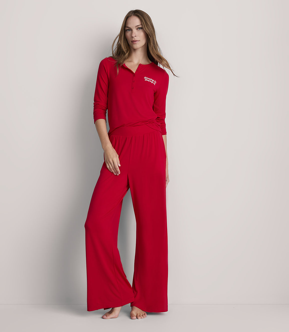 A woman in red pajamas stands against a plain, light gray background.