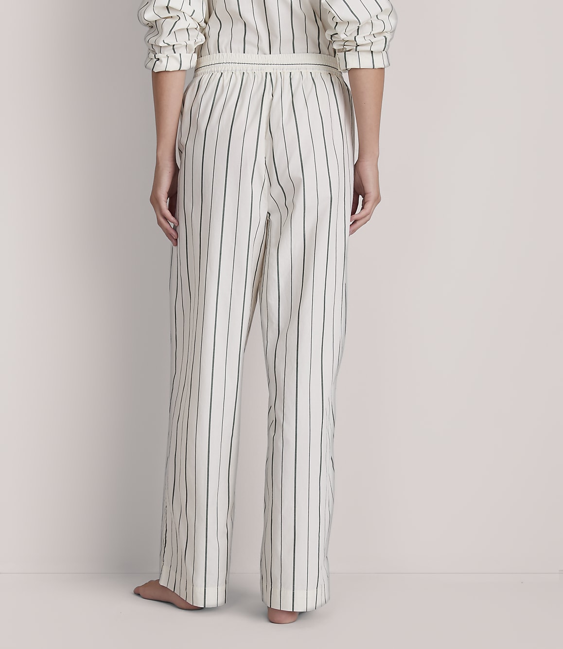 A person stands in striped pajamas against a plain, light-colored background.