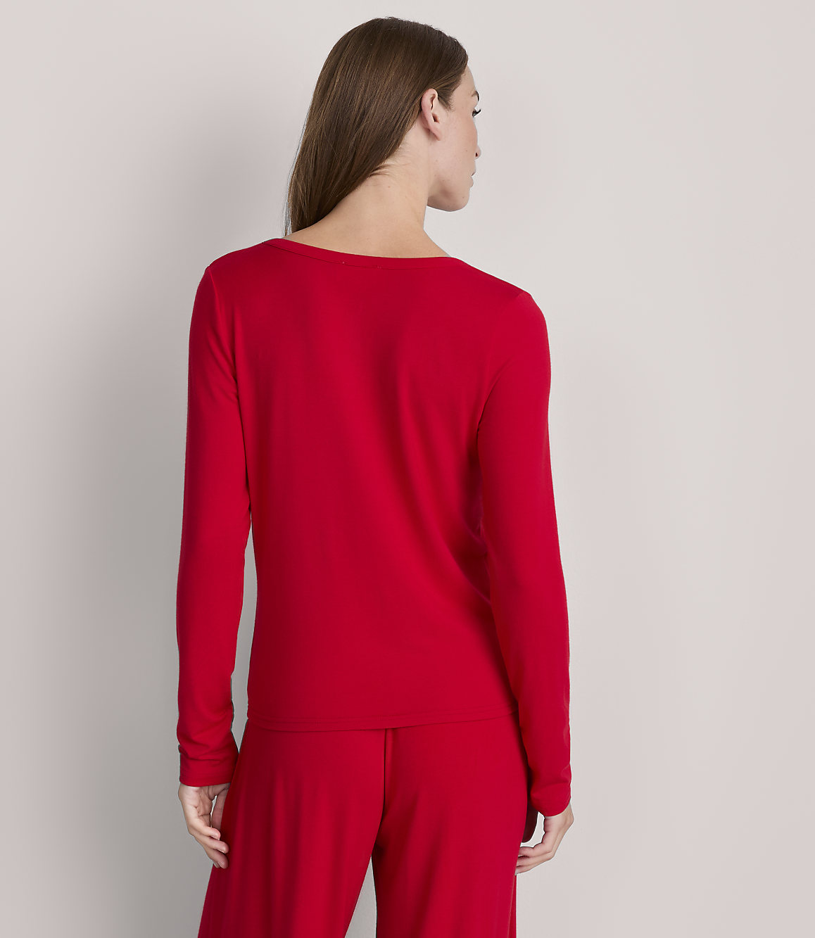 A woman in a red long-sleeved shirt and pants stands against a plain gray background.