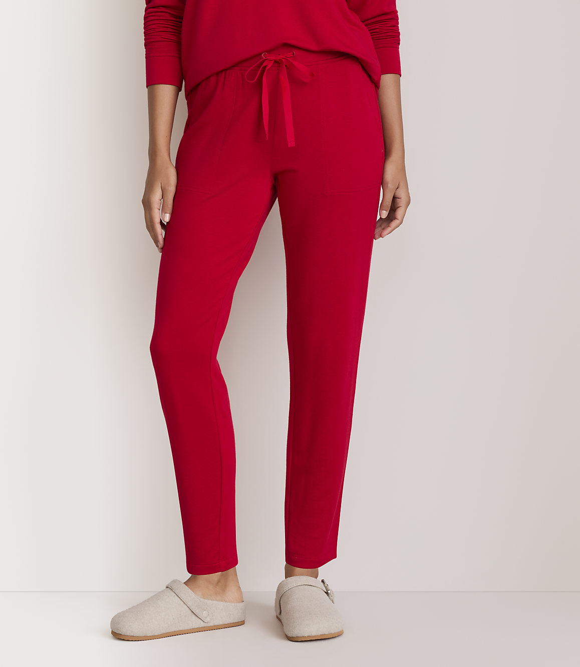 A person wearing red pajama pants and beige slippers stands against a plain white background.
