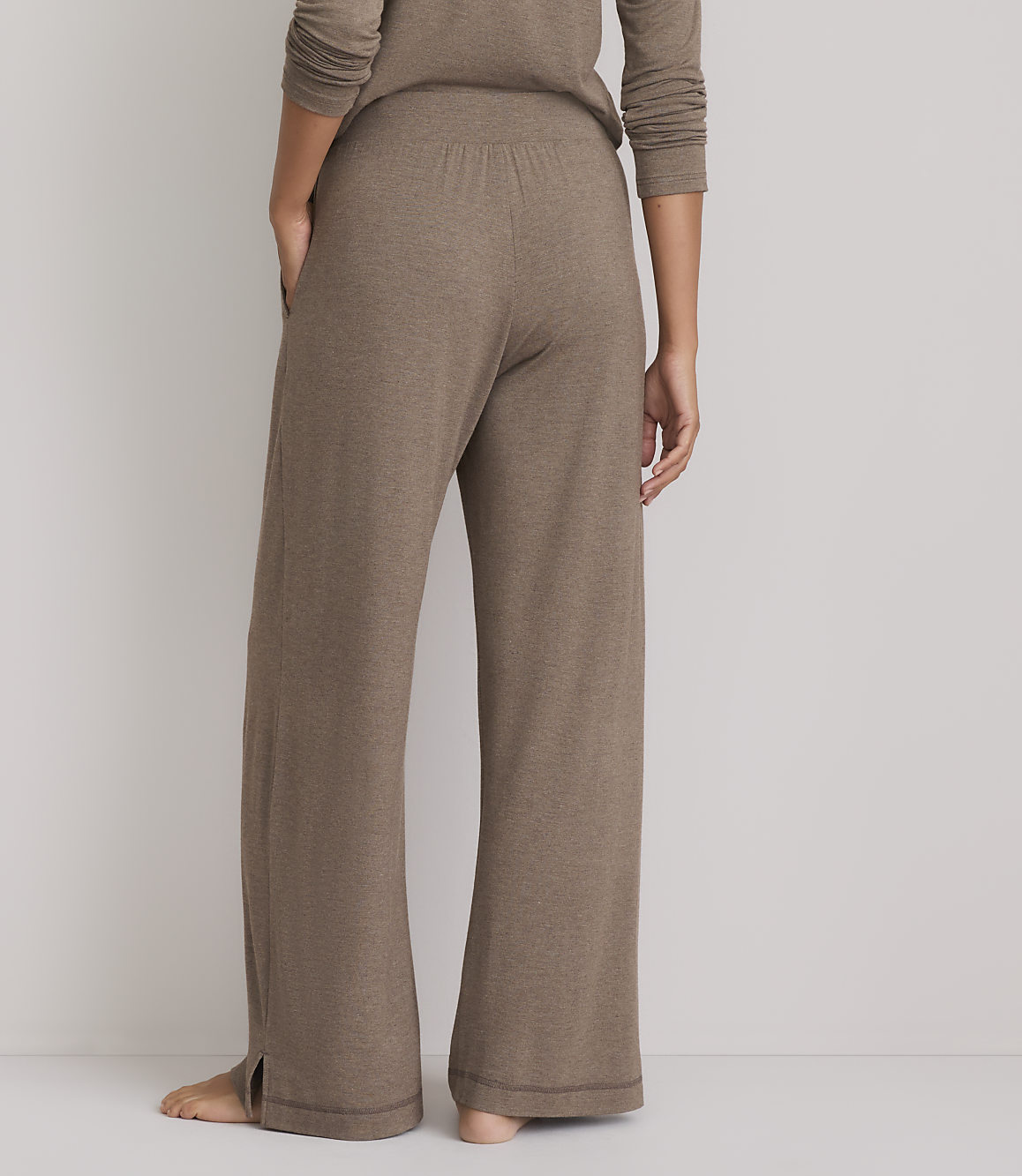A person wearing brown lounge pants with a split hem stands against a plain gray background.
