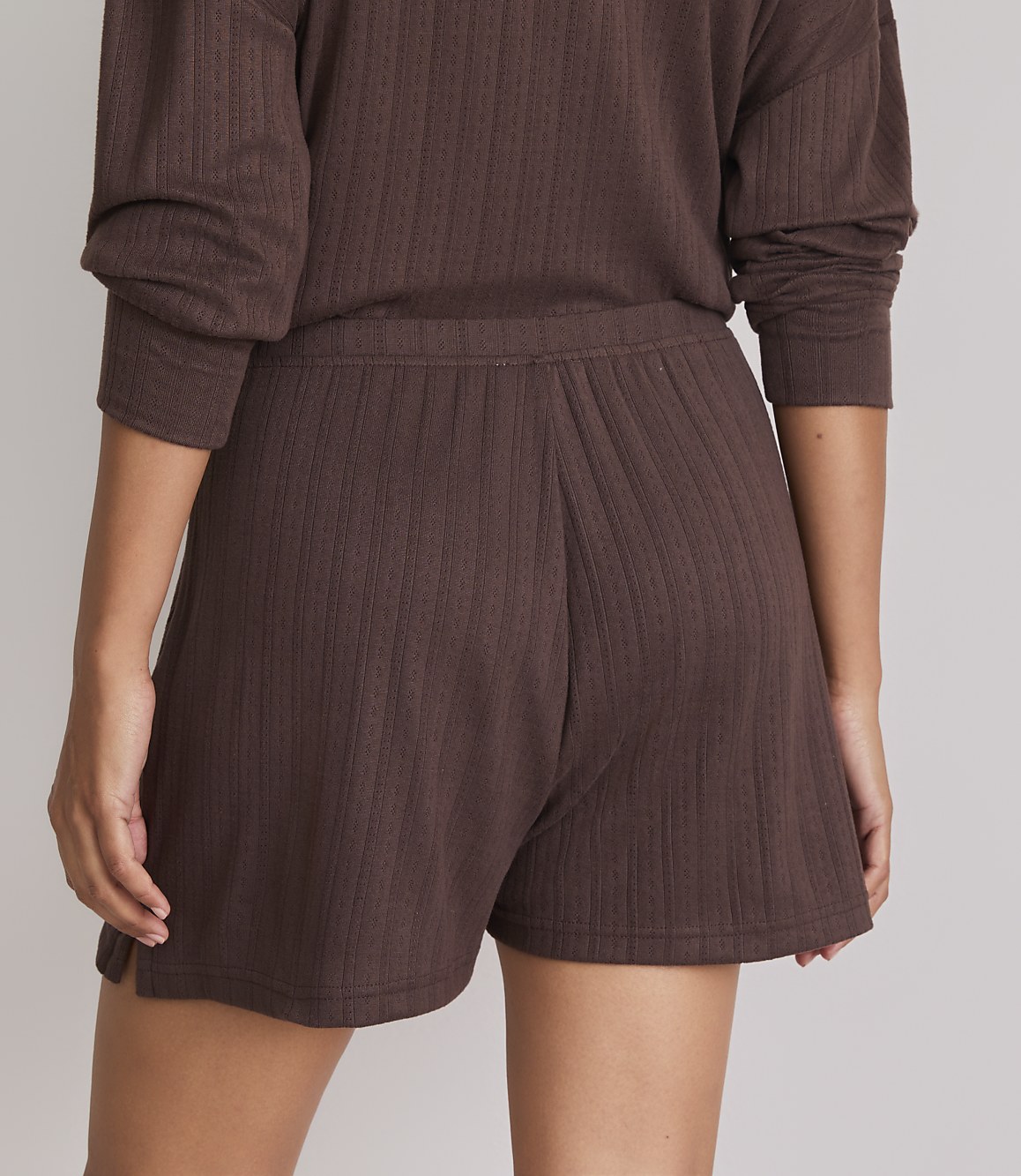A person wearing brown ribbed shorts and a matching top stands against a plain background.
