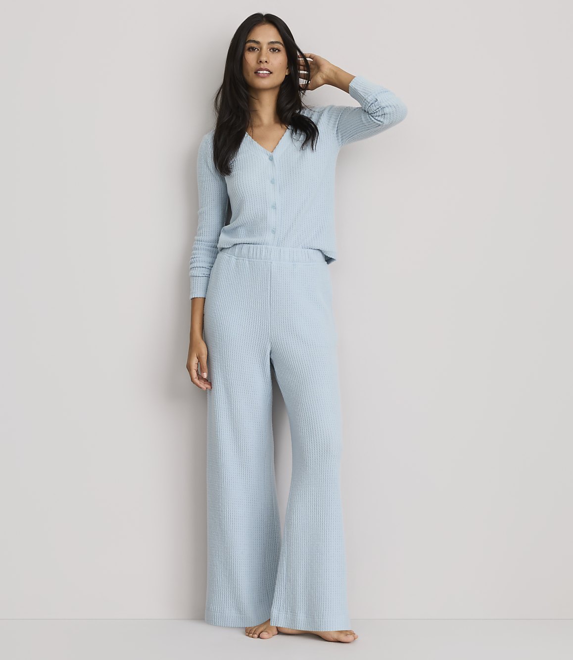 A woman in light blue ribbed pajamas stands against a plain, light gray background.