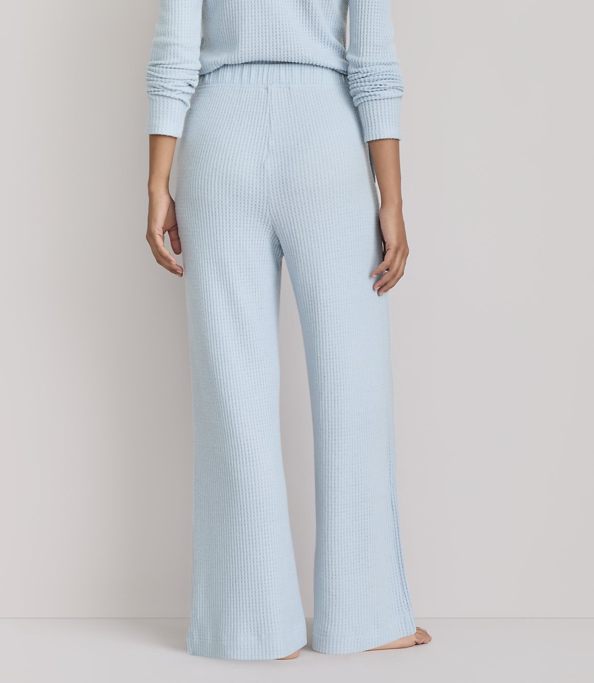 A person stands in light blue waffle-knit pajamas against a plain, light gray background.