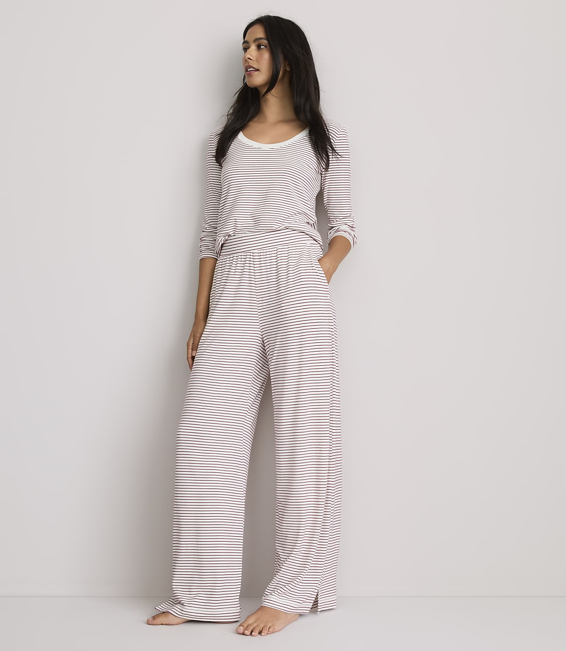 A woman in striped pajamas stands against a plain, light-colored wall.