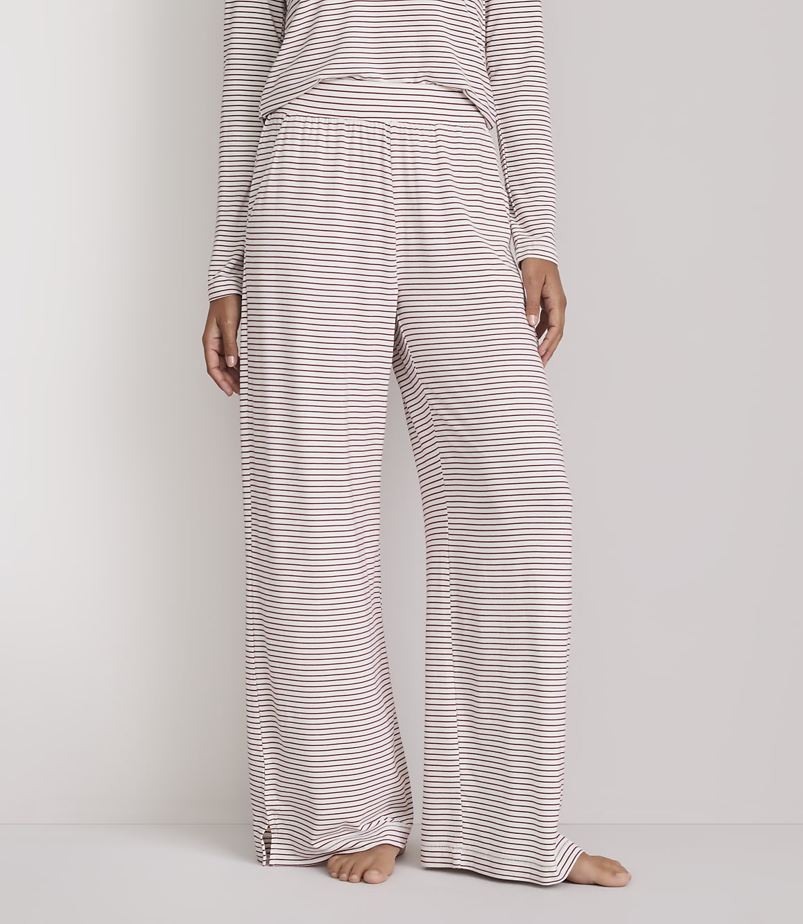 A person stands wearing striped pajama pants and a matching top against a plain white background.