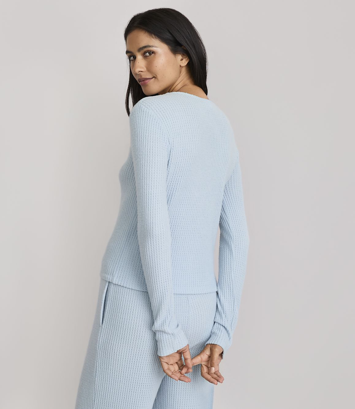 A woman in a light blue ribbed top and pants stands against a plain gray background.