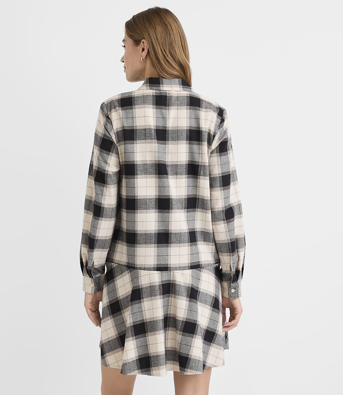 A woman in a plaid shirt and skirt stands against a plain white background.