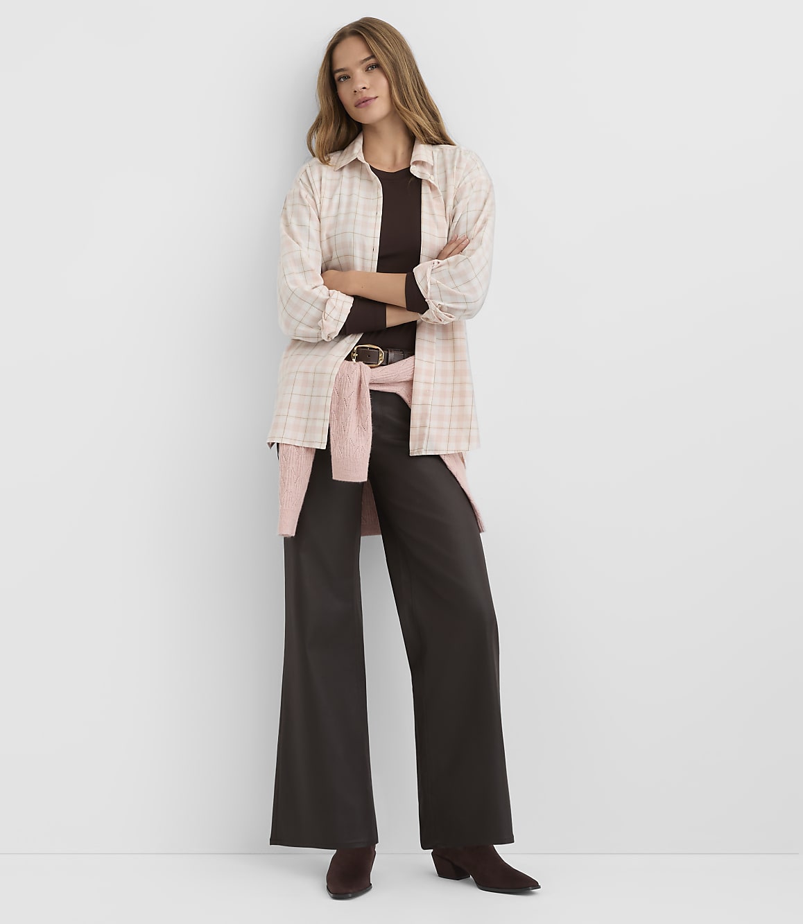 A woman in a plaid shirt and wide-leg pants stands against a plain white background.