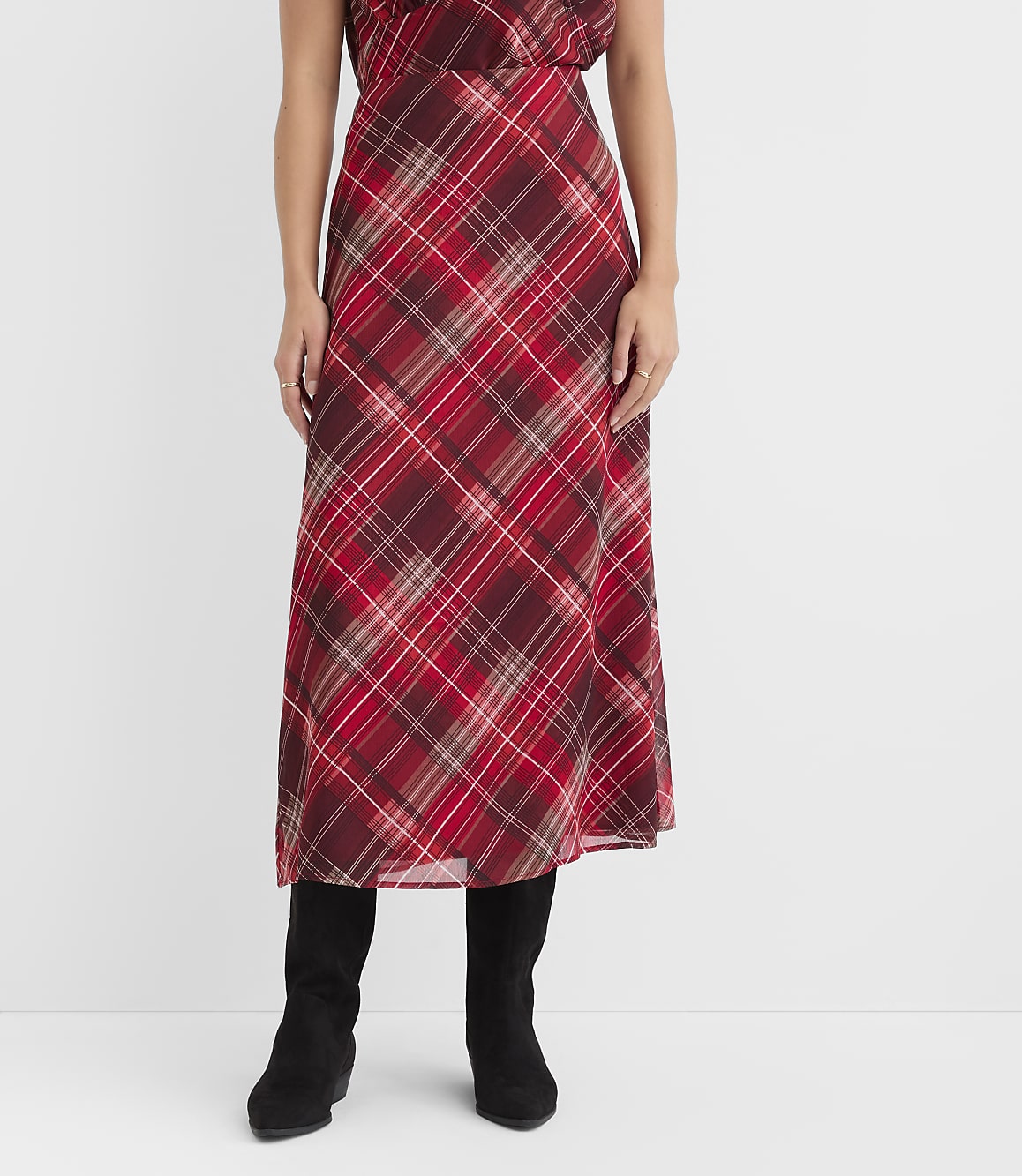 A woman in a red plaid skirt and black boots stands against a plain white background.