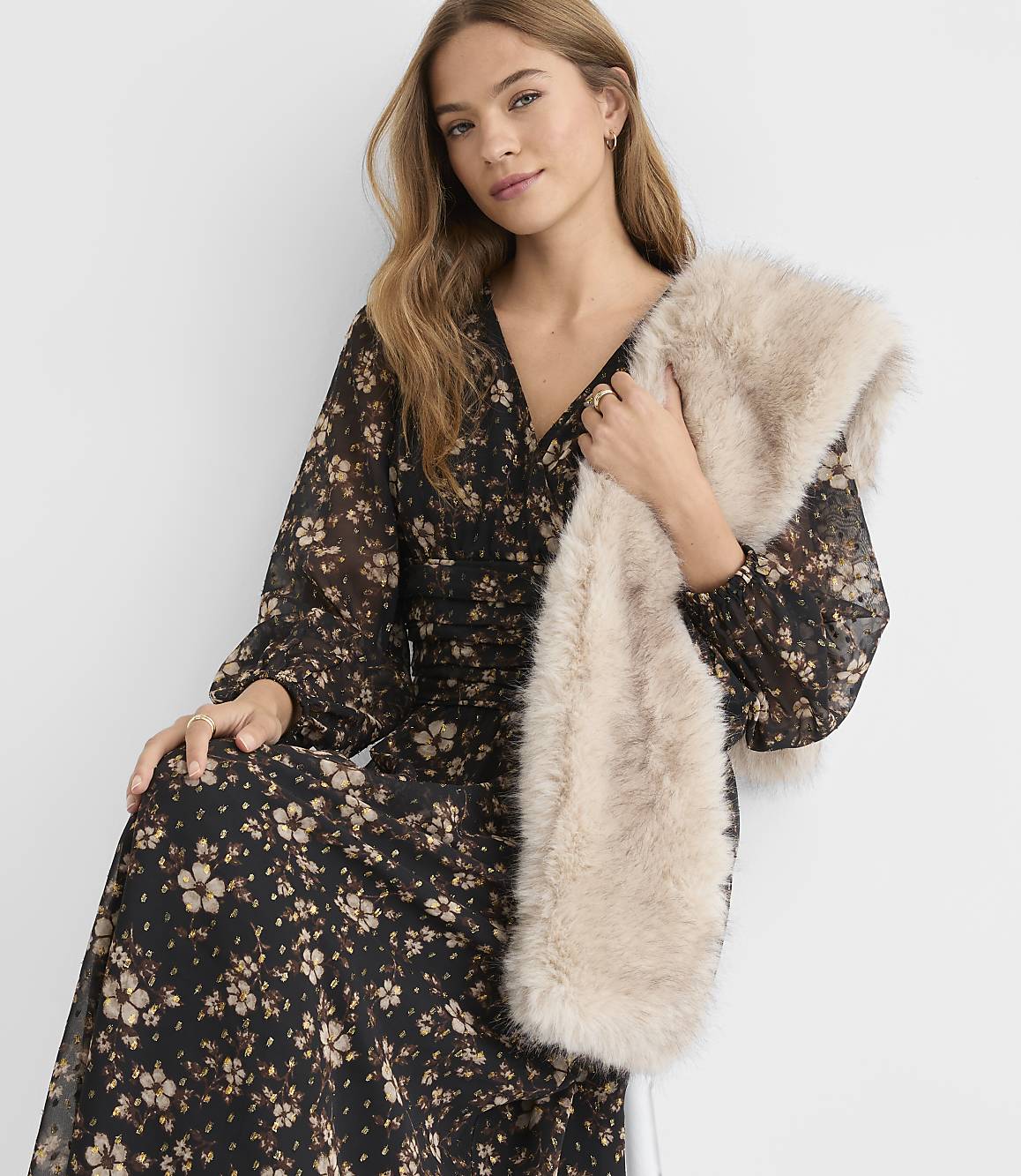 A woman in a floral dress holds a fluffy faux fur stole in front of a plain white background.