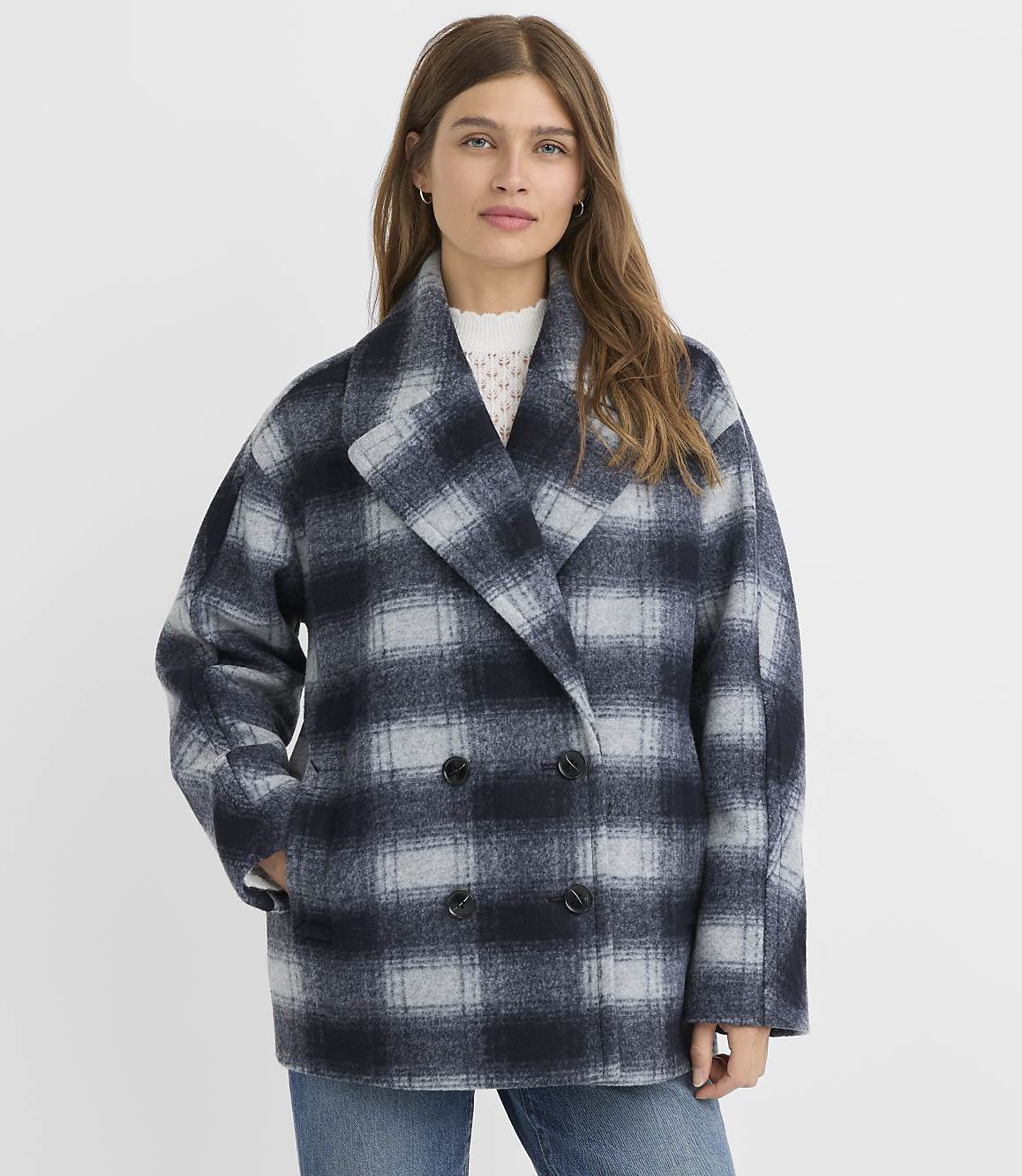 A woman in a plaid coat stands against a plain white background.